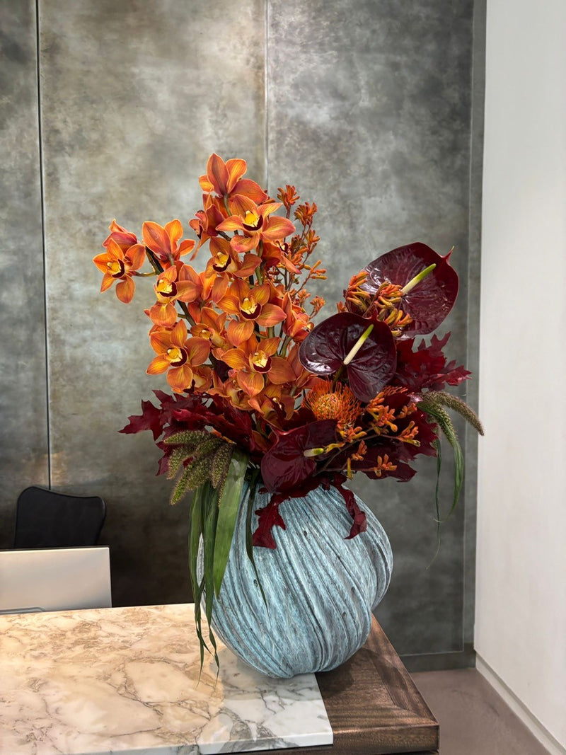 Decorative floral arrangement in a textured vase on a marble surface with a metallic wall background.
