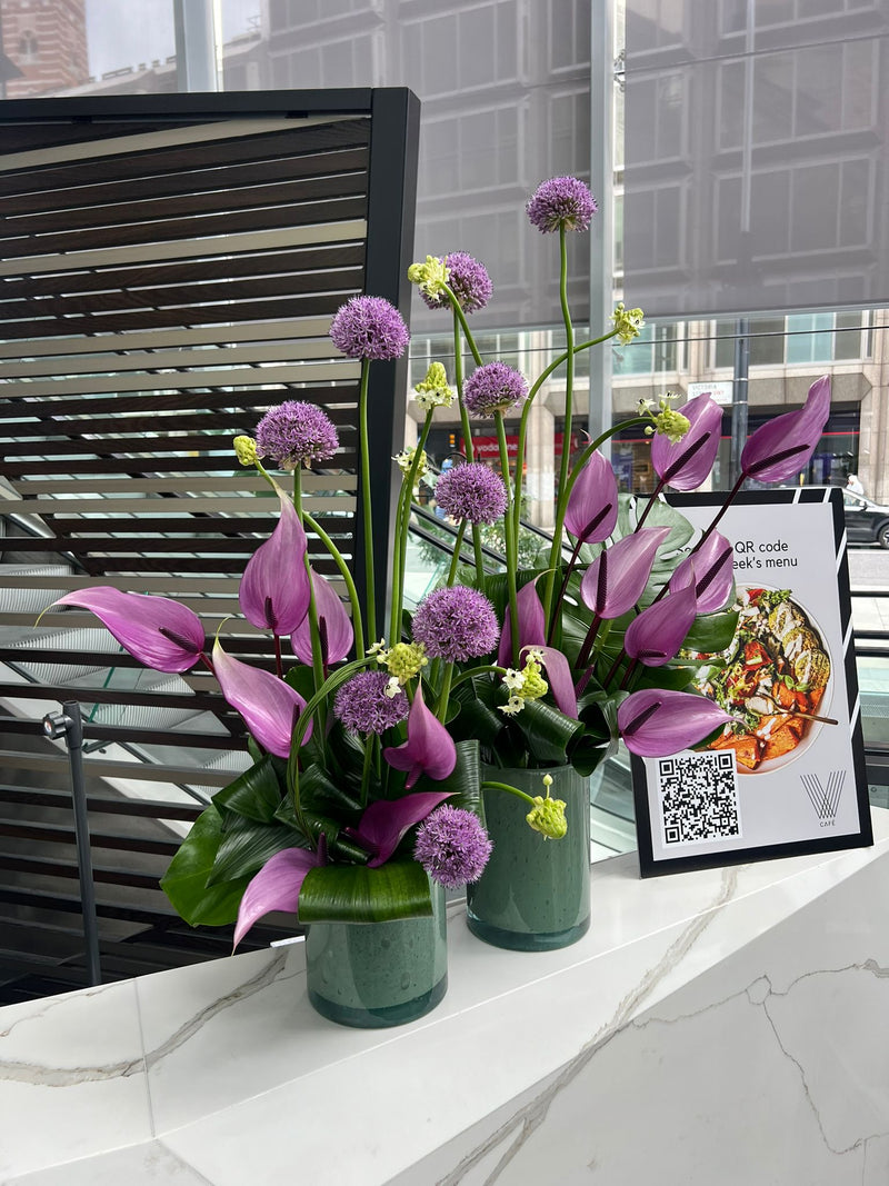 Floral arrangement with purple flowers in green vases in london office