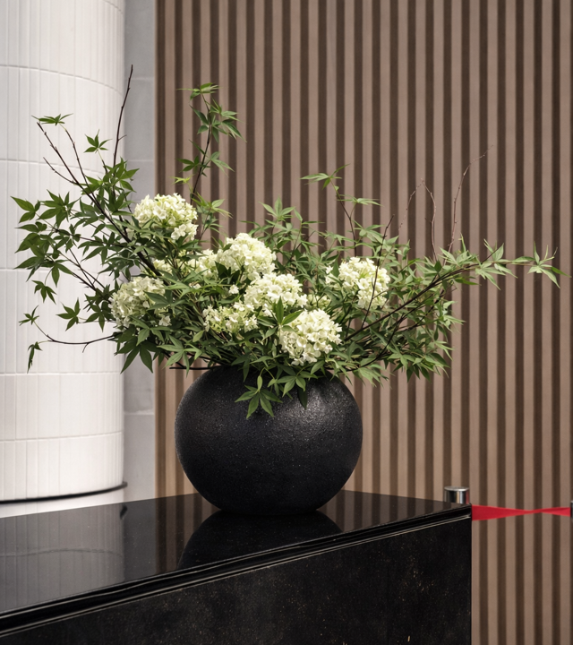 Black vase with white flowers and green leaves in london office reception